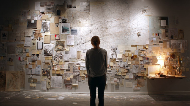 Personne observant un mur de notes et de repères, symbolisant l’exploration et la cartographie des lieux culturels.